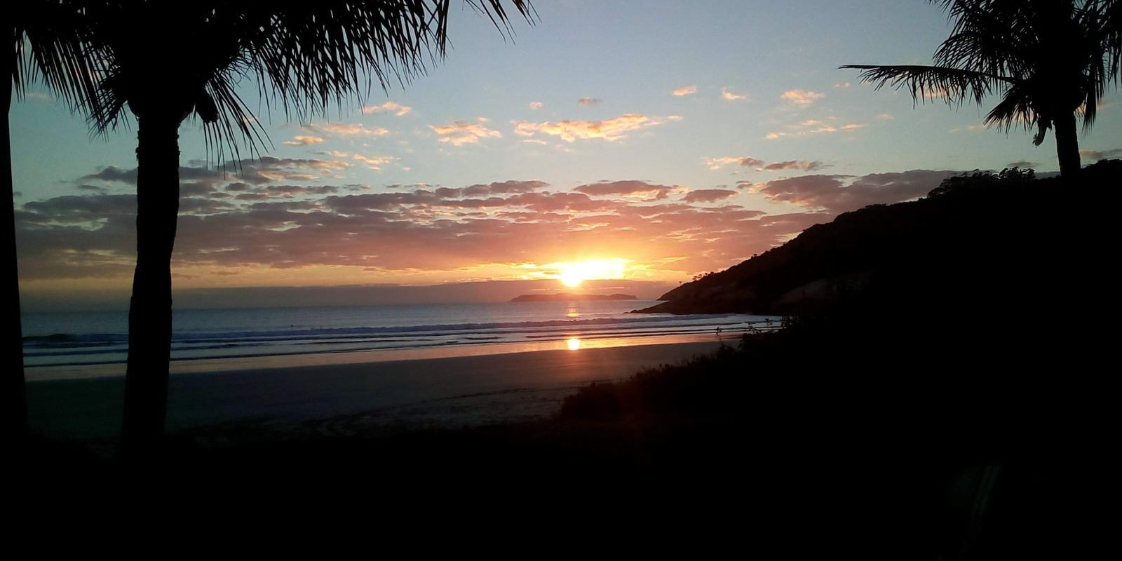 Vista aérea da península de Bombinhas ao entardecer, com praias pequenas, mar claro e vegetação preservada