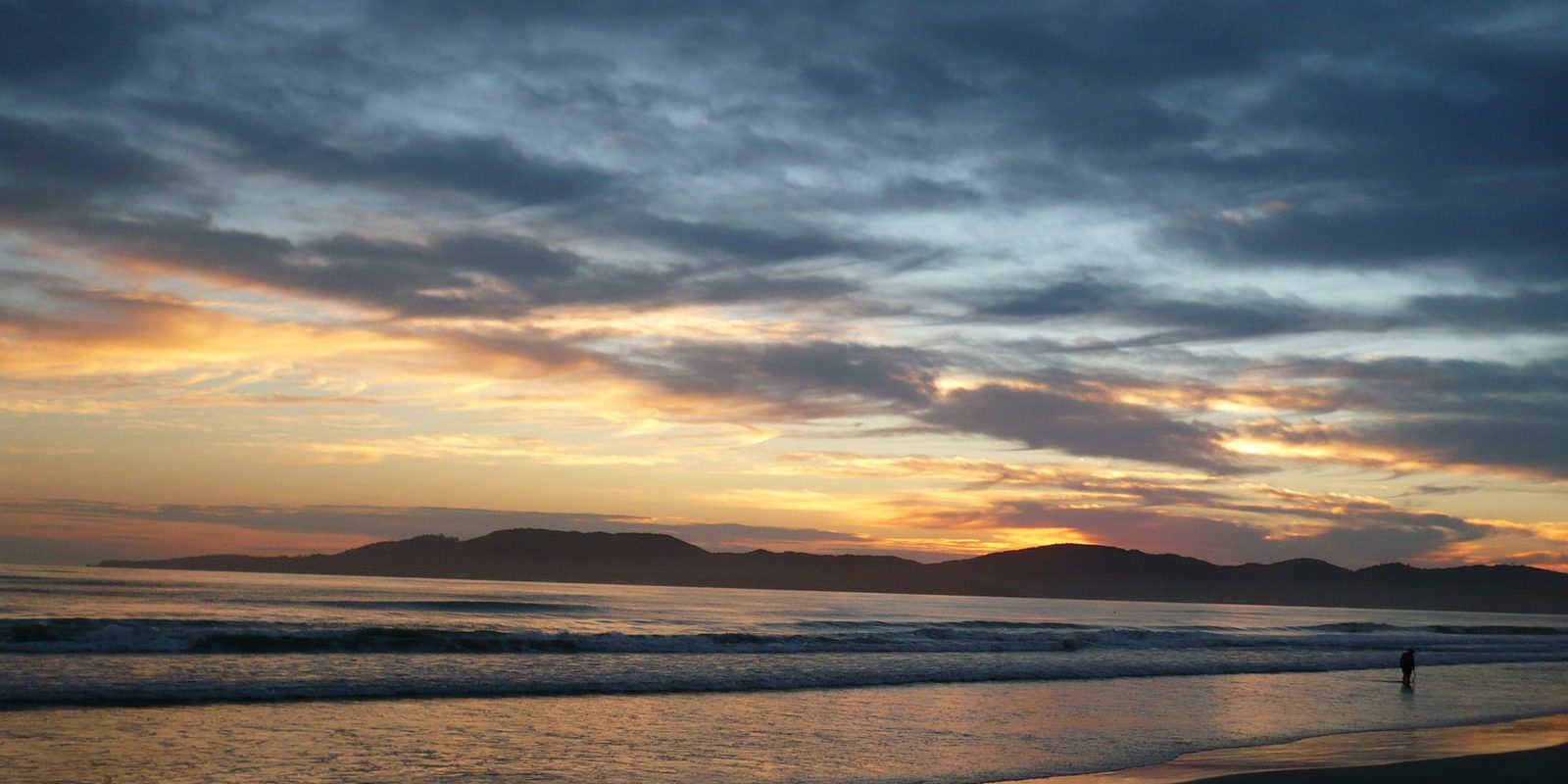 Vista aérea da orla verticalizada de Itapema ao entardecer, com a praia extensa e as torres à beira-mar