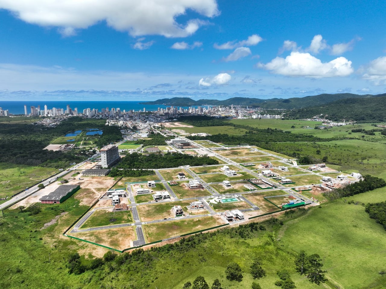 Vista aérea real das obras em Porto Belo, com a cidade e o litoral ao fundo